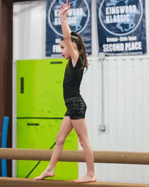Young gymnast performing perfect form on balance beam with expert coach guidance